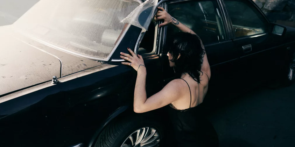 Eine Person kniet vor einem schwarzen Auto.