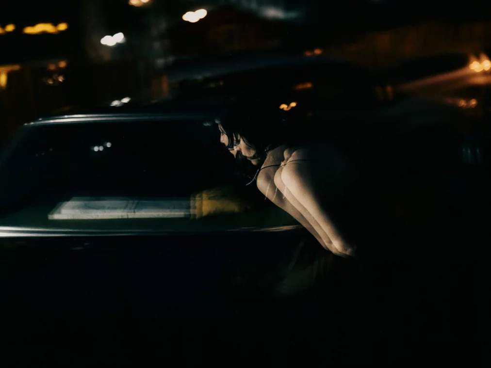 Blurred lights and the silhouettes of a person and a car can be seen in a dark picture. 