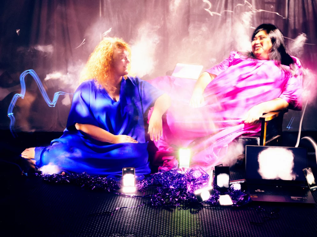 Two people in colorful dresses sit and look at each other.