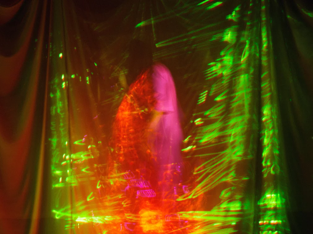 Green lights are projected onto a transparent cloth hanging from the ceiling. The silhouette of a person can be seen behind it.