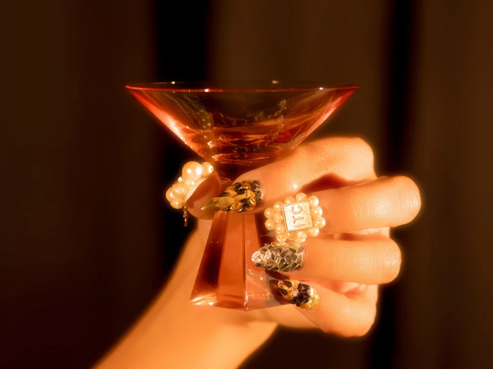 Close-up of a hand holding a red cocktail glass, with long decorated fingernails.