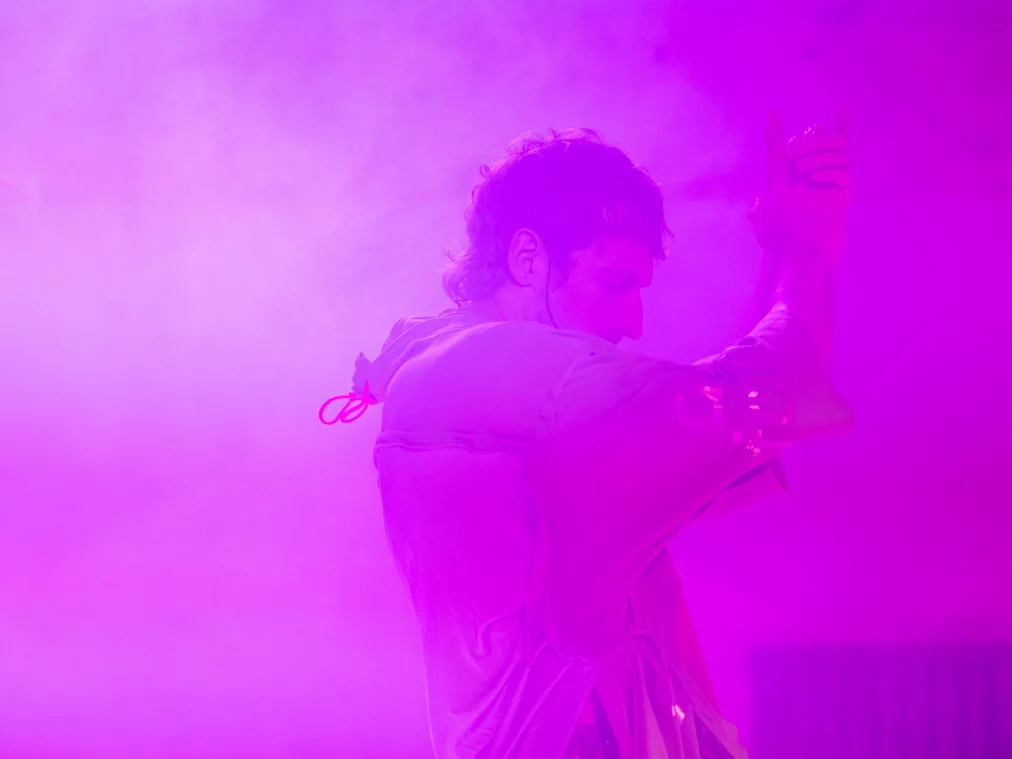 Eine Person tanzt oder bewegt sich langsam in dichtem pinkem Nebel. Das Gesicht ist im Profil zu sehen, der Körper von intensivem Magenta-Licht umhüllt. Die Szene wirkt traumartig und weich.