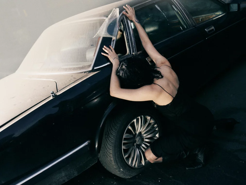 Eine Person kniet vor einem schwarzen Auto.