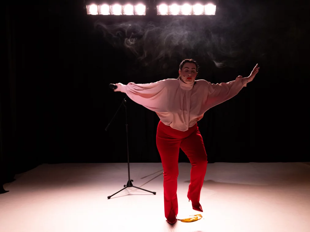 A person moves across the stage with arms outstretched, stepping close to a banana peel on the floor.