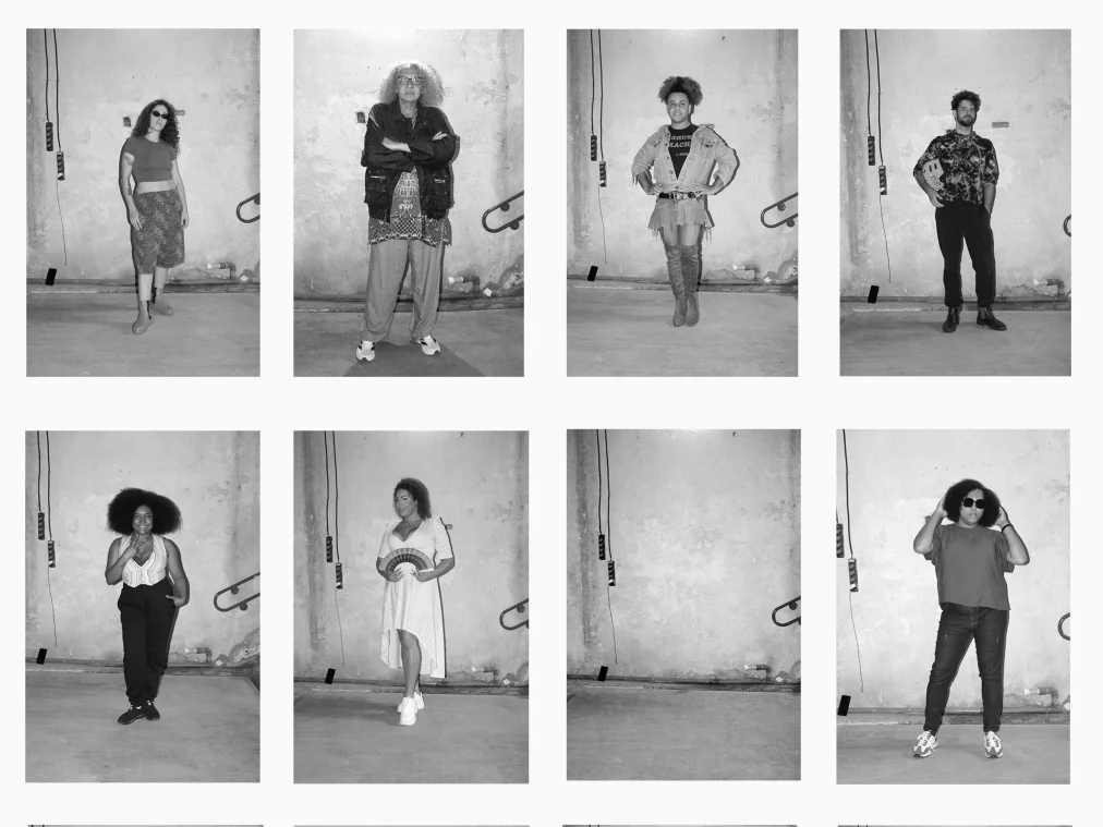 Eine Collage aus zwölf schwarz-weißen Porträtfotografien zeigt verschiedene Personen einzeln vor einer rauen Wand in einem leeren Innenraum. Die Personen nehmen unterschiedliche Posen ein: einige stehen mit verschränkten Armen oder Händen in den Hüften, andere tragen Sonnenbrillen oder blicken direkt in die Kamera. Zwei Felder der Collage bleiben leer und zeigen nur die Wand und den Boden des Raumes. Die Aufnahmen wirken wie dokumentarische Studio- oder Castingporträts.